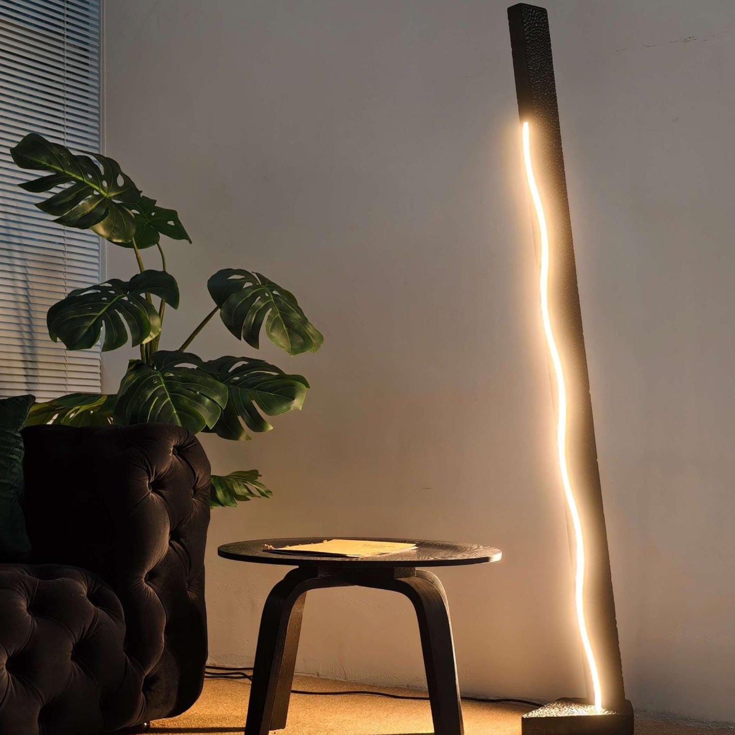 Modern floor lamp casting light on a plant and table in a room.
