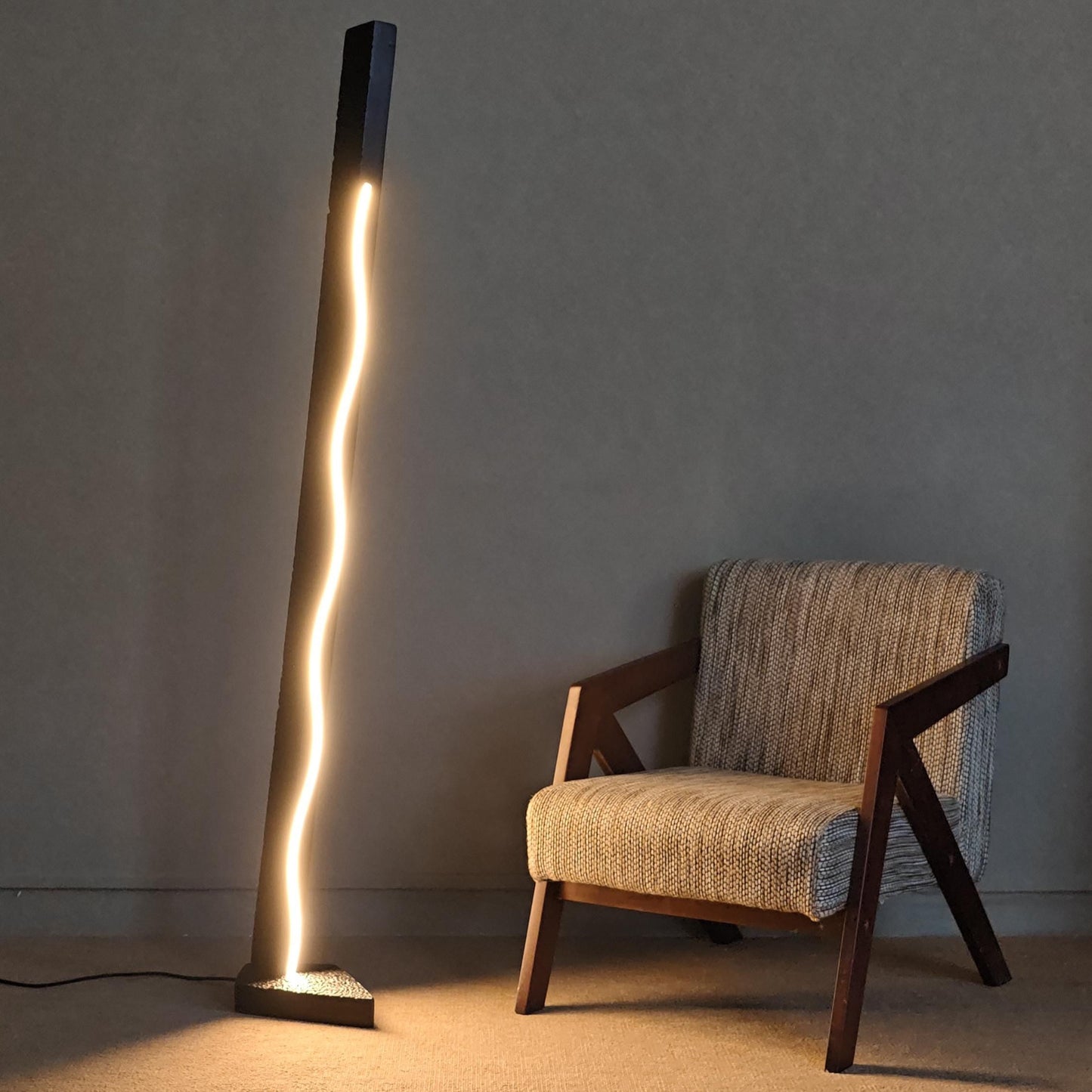 Tall floor lamp with a warm glow next to a textured armchair against a plain wall.