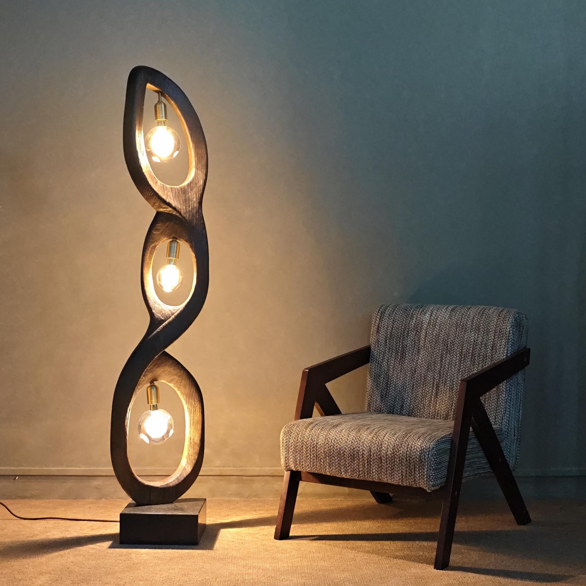 Modern floor lamp with spiral design next to a chair against a plain wall.