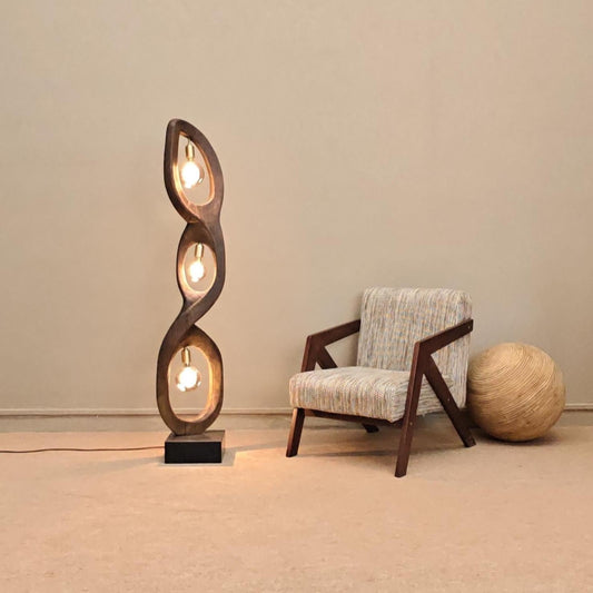 Wooden spiral floor lamp next to a chair and decorative ball on a beige carpet.