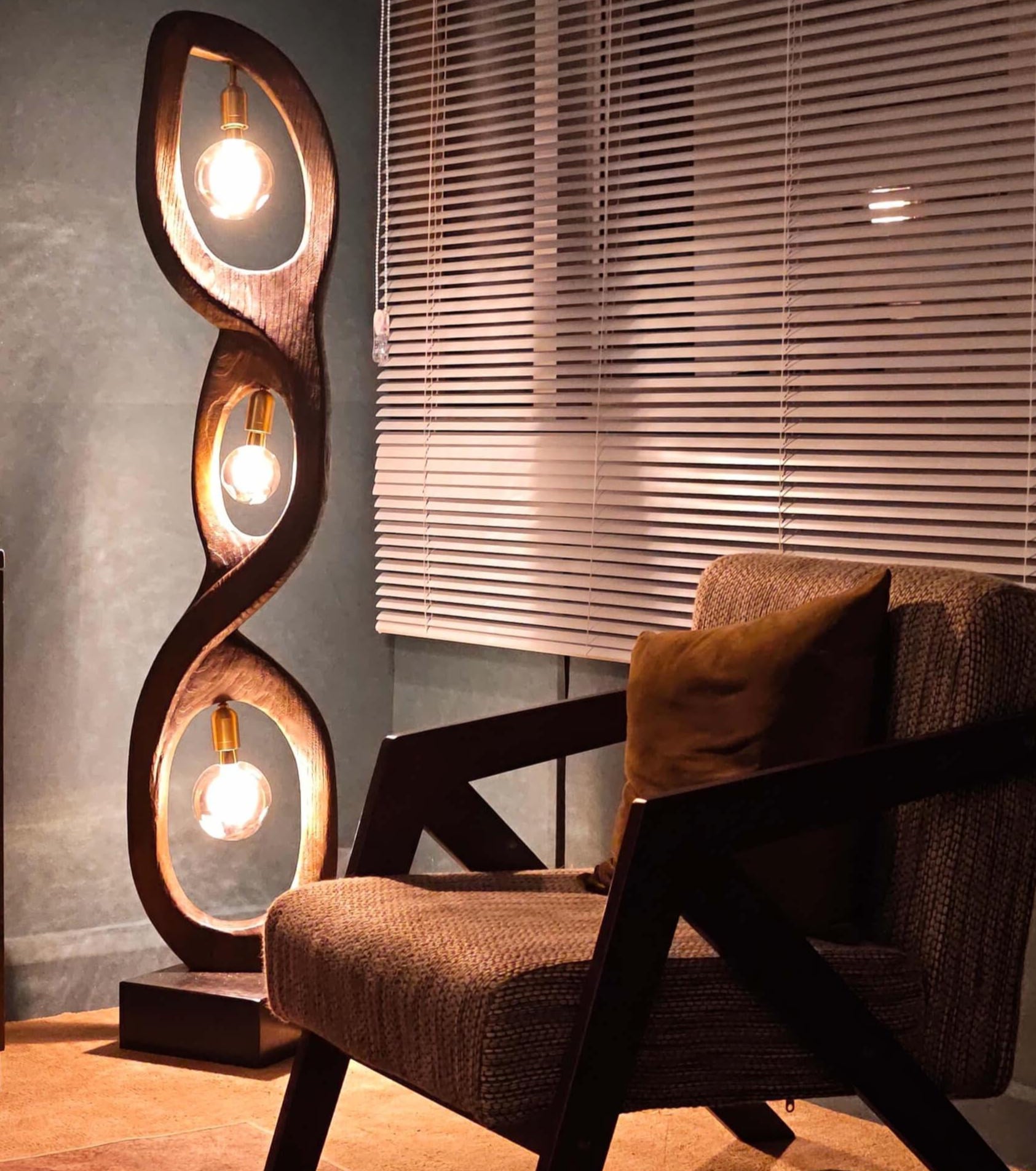 Modern floor lamp with three light bulbs in a room with a chair and window blinds.