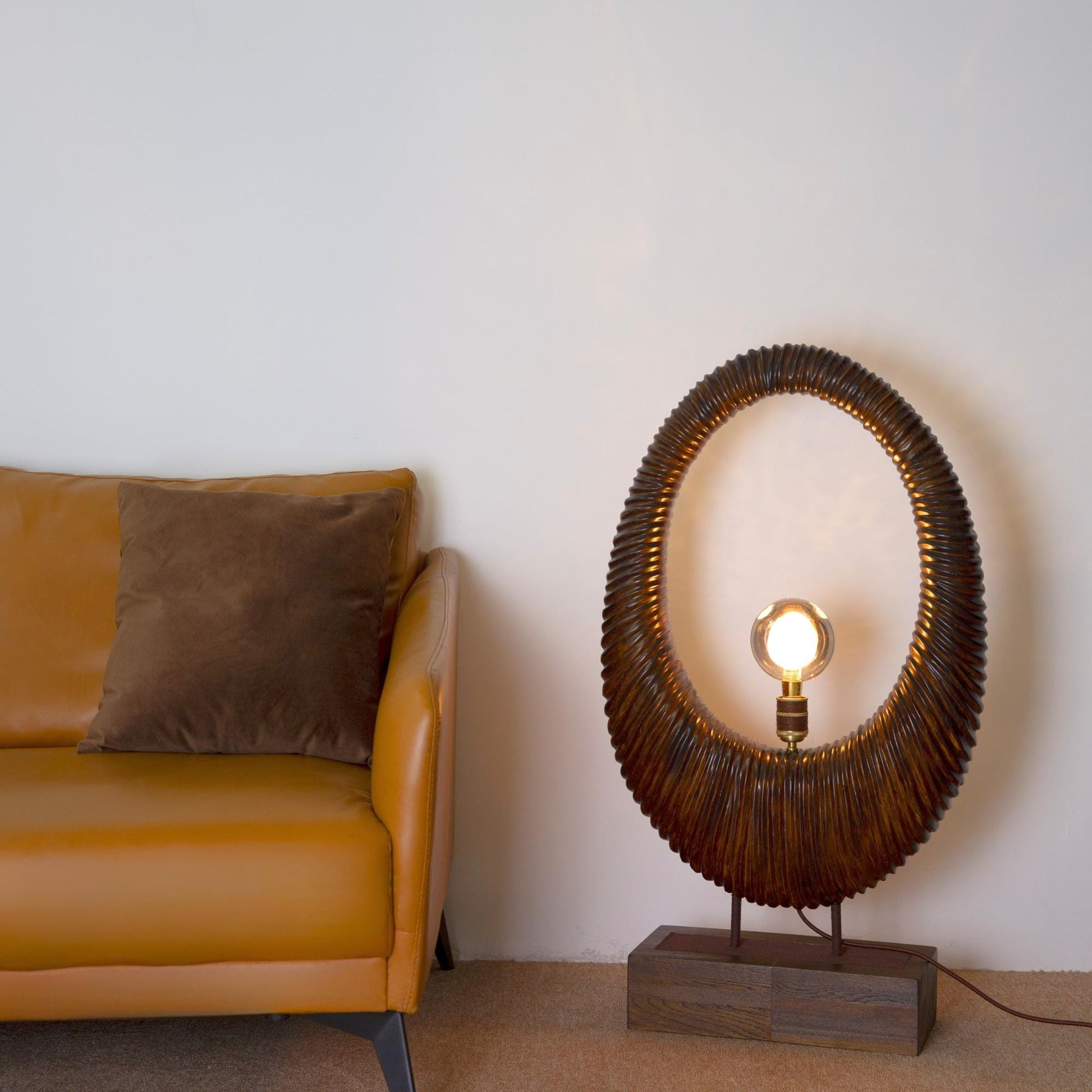 Wicker lamp with light bulb on a wooden base next to a yellow sofa against a white wall.
