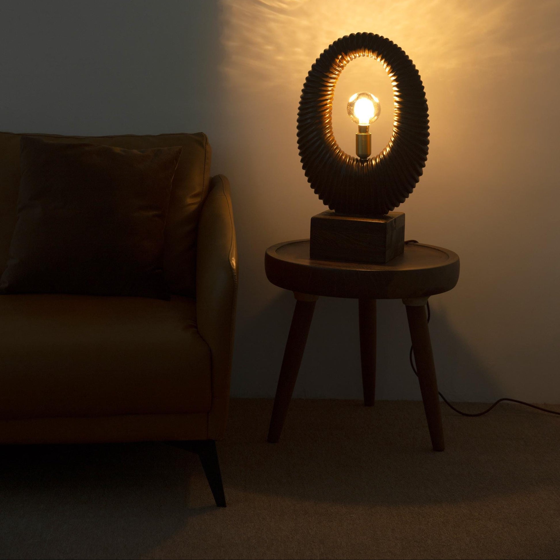 Table lamp with a unique design on a small round table in a dimly lit room.